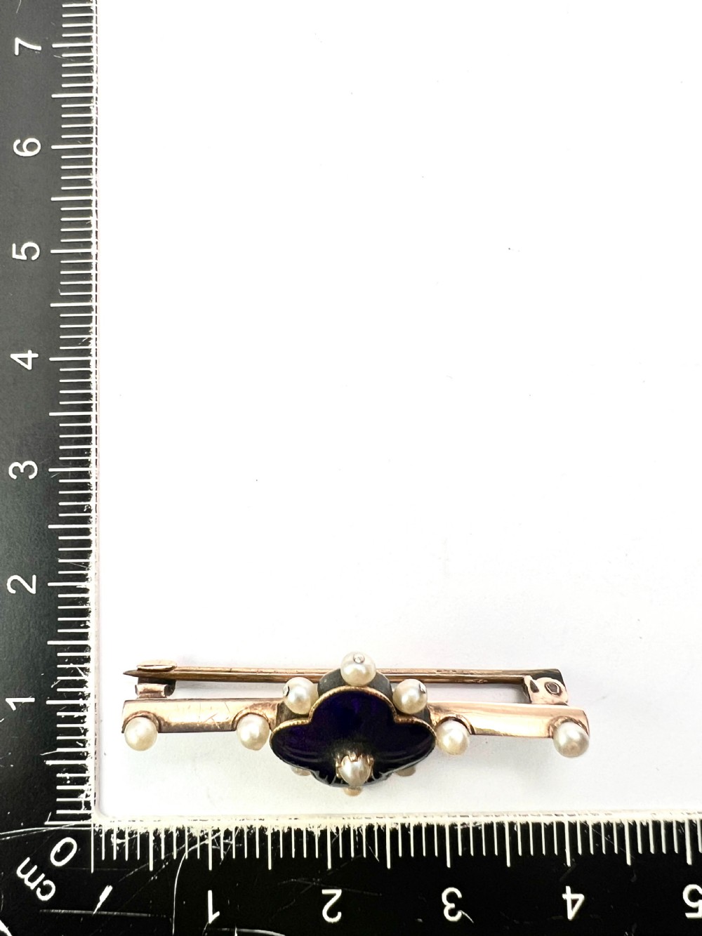 An Edwardian gold bar brooch featuring a central quatrefoil motif decorated in cobalt blue guilloche enamel and surrounded by pearls. View VIII