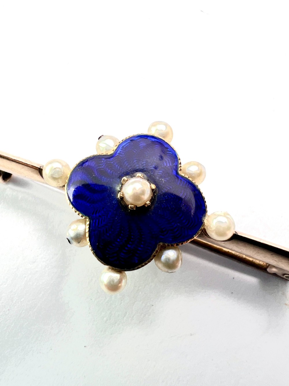 An Edwardian gold bar brooch featuring a central quatrefoil motif decorated in cobalt blue guilloche enamel and surrounded by pearls. View IX
