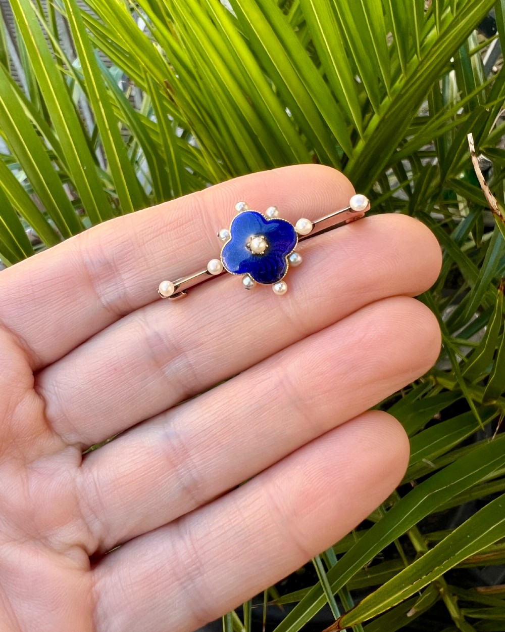 An Edwardian gold bar brooch featuring a central quatrefoil motif decorated in cobalt blue guilloche enamel and surrounded by pearls. View X