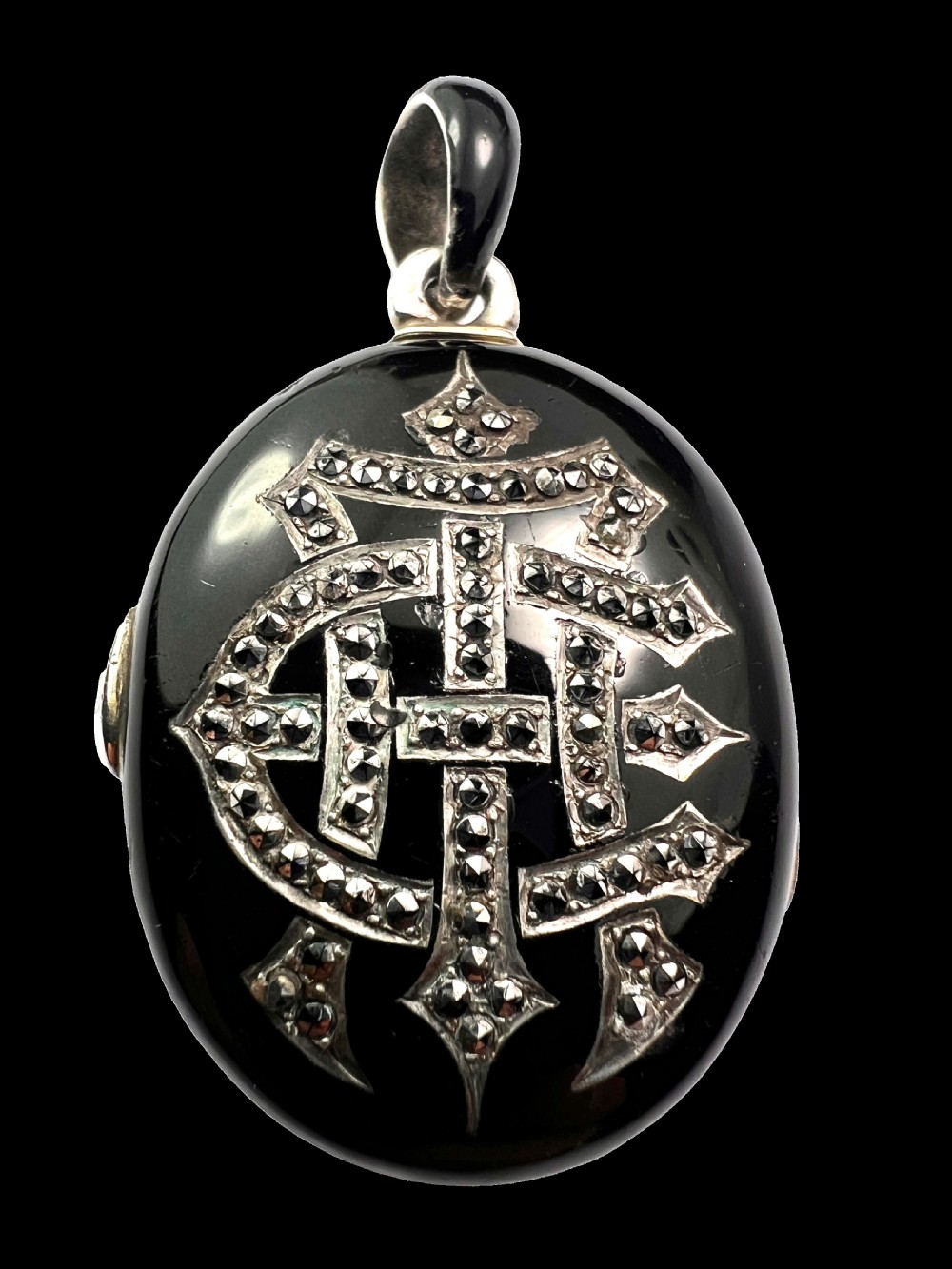 An oval Victorian silver locket rendered in black enamel with an intricate marcasite-set AEI monogram on the front surface. View II