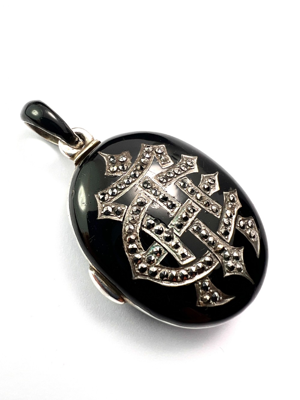 An oval Victorian silver locket rendered in black enamel with an intricate marcasite-set AEI monogram on the front surface. View III