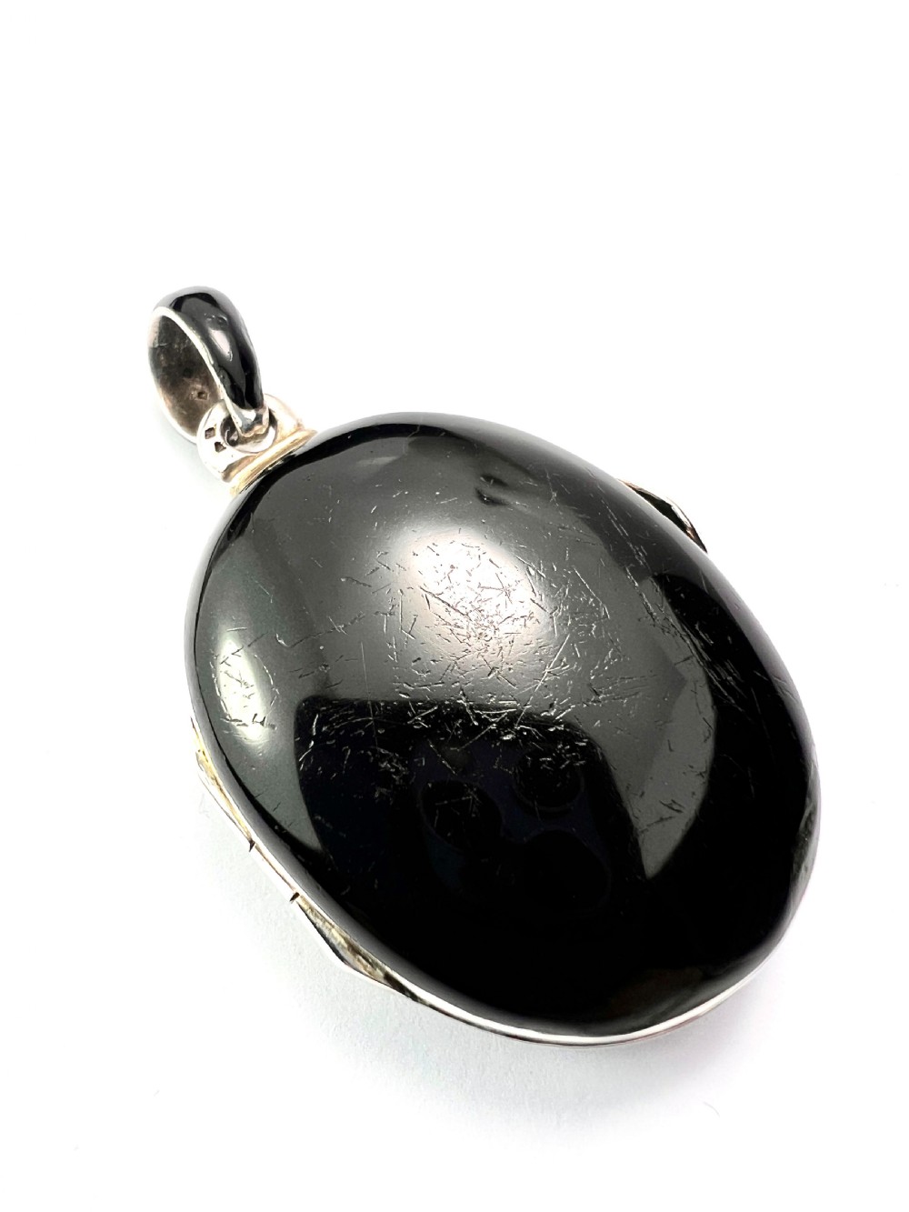 An oval Victorian silver locket rendered in black enamel with an intricate marcasite-set AEI monogram on the front surface. View IV