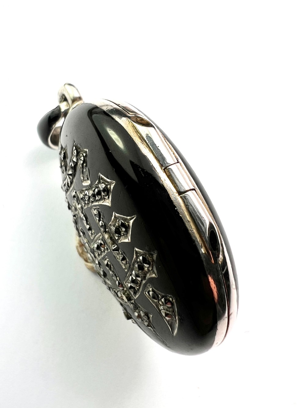 An oval Victorian silver locket rendered in black enamel with an intricate marcasite-set AEI monogram on the front surface. View VII