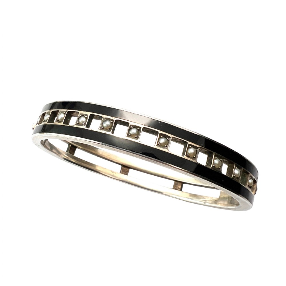 An antique Austro-Hungarian silver hinged bangle featuring black enamel borders and an openwork centre set with seed pearls.
