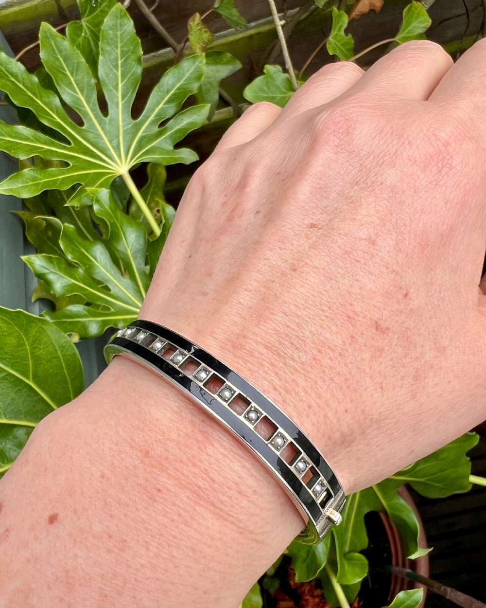 An antique Austro-Hungarian silver hinged bangle featuring black enamel borders and an openwork centre set with seed pearls. View VII