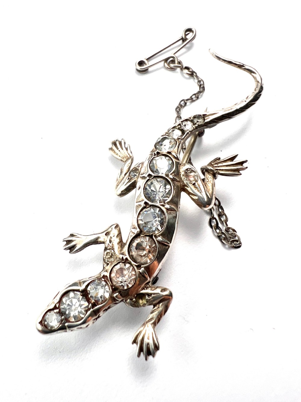 An Art Deco silver brooch shaped like a lizard, encrusted with round clear paste stones along its spine and head, featuring an attached safety chain. View II