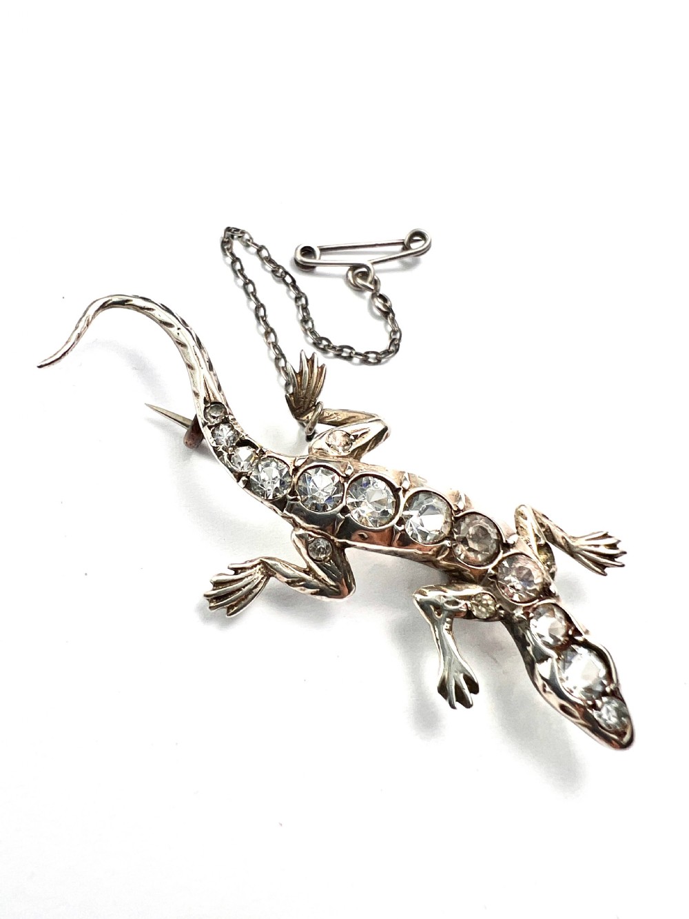 An Art Deco silver brooch shaped like a lizard, encrusted with round clear paste stones along its spine and head, featuring an attached safety chain. View III