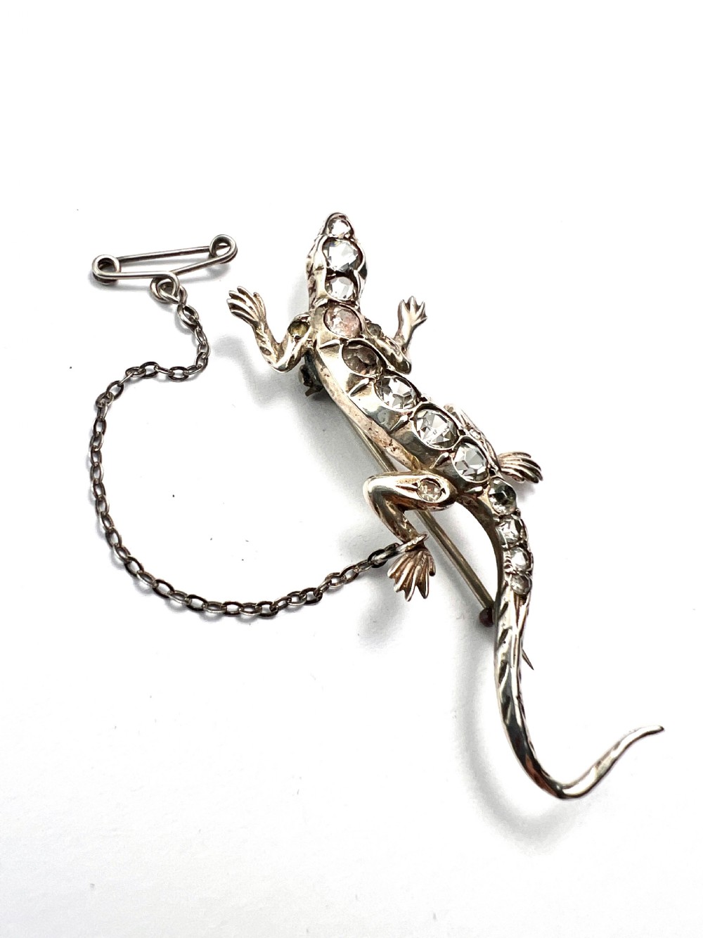 An Art Deco silver brooch shaped like a lizard, encrusted with round clear paste stones along its spine and head, featuring an attached safety chain. View IV