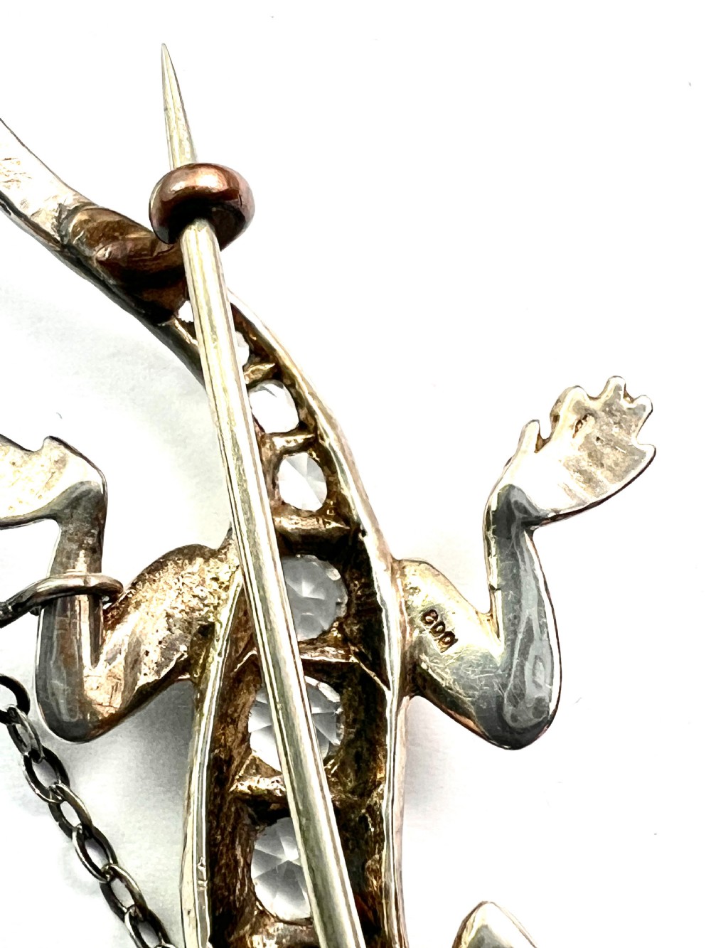 An Art Deco silver brooch shaped like a lizard, encrusted with round clear paste stones along its spine and head, featuring an attached safety chain. View V