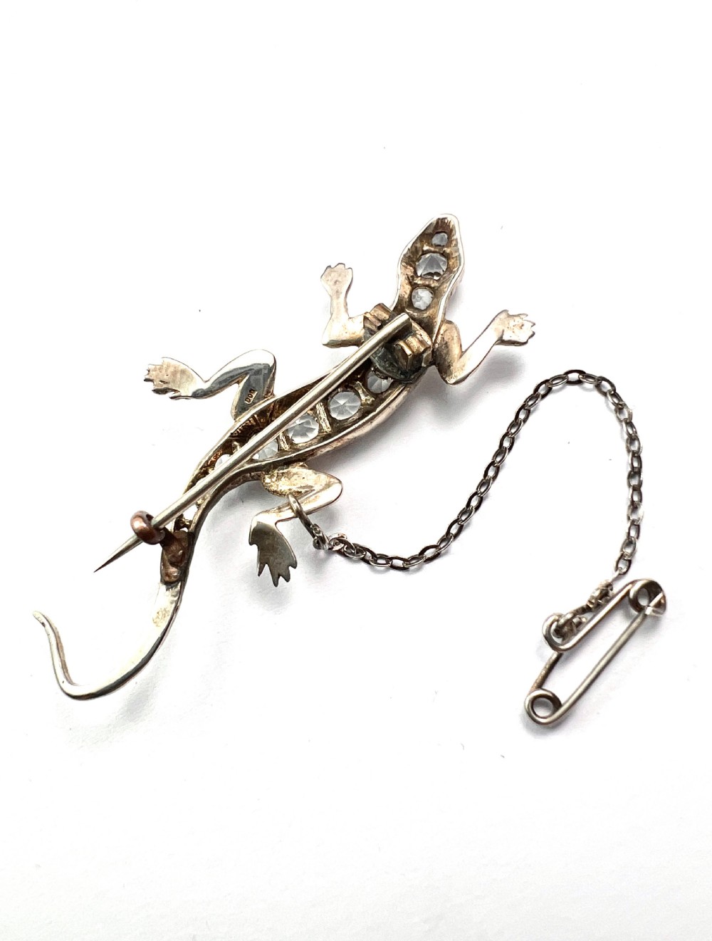 An Art Deco silver brooch shaped like a lizard, encrusted with round clear paste stones along its spine and head, featuring an attached safety chain. View VI