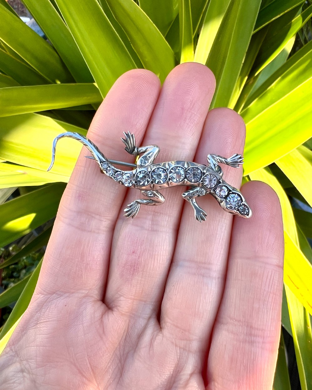 An Art Deco silver brooch shaped like a lizard, encrusted with round clear paste stones along its spine and head, featuring an attached safety chain. View VIII