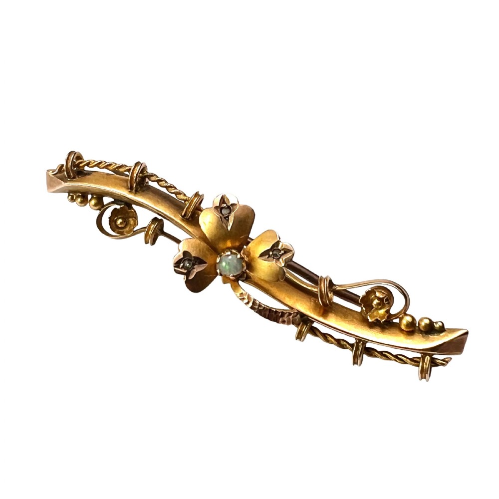 A Victorian 9ct yellow gold bar brooch featuring a central three-leaf clover set with a cabochon opal and accent diamonds.