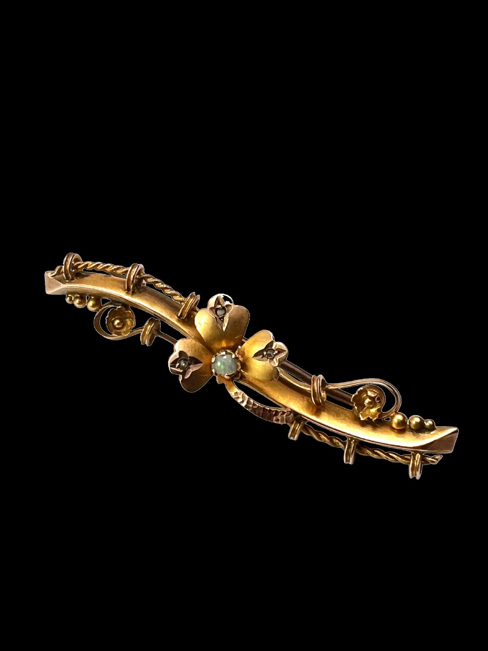 A Victorian 9ct yellow gold bar brooch featuring a central three-leaf clover set with a cabochon opal and accent diamonds. View V