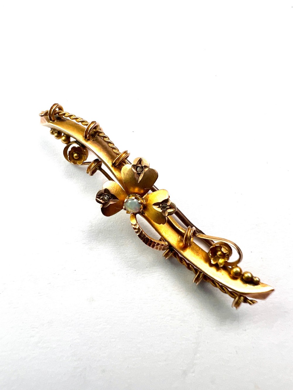 A Victorian 9ct yellow gold bar brooch featuring a central three-leaf clover set with a cabochon opal and accent diamonds. View VII
