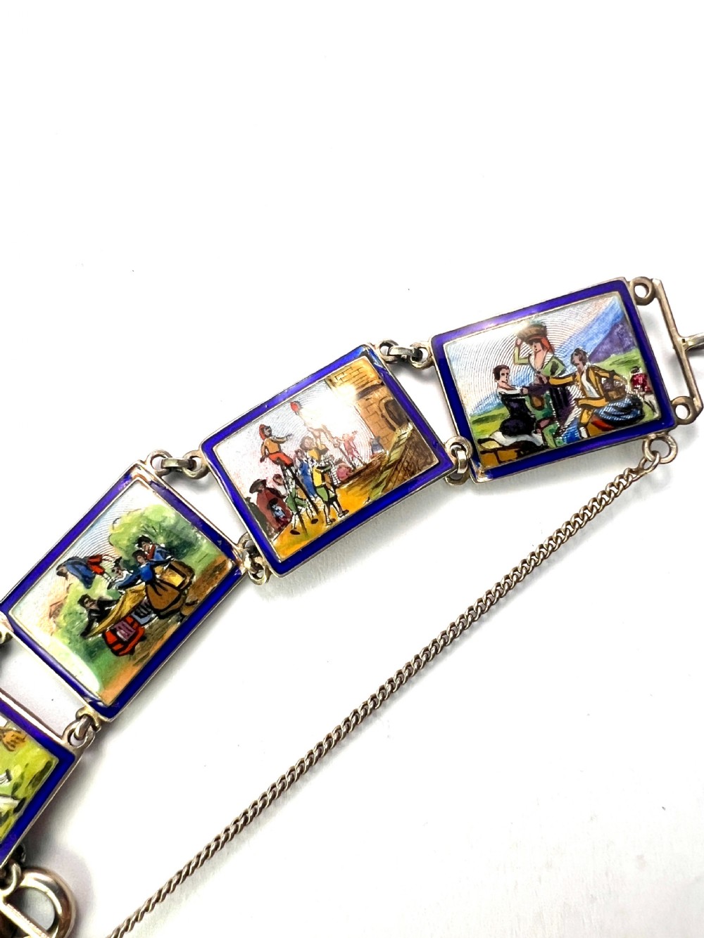 A vintage silver link bracelet featuring rectangular panels decorated with hand-painted miniature genre scenes bordered in cobalt blue enamel.