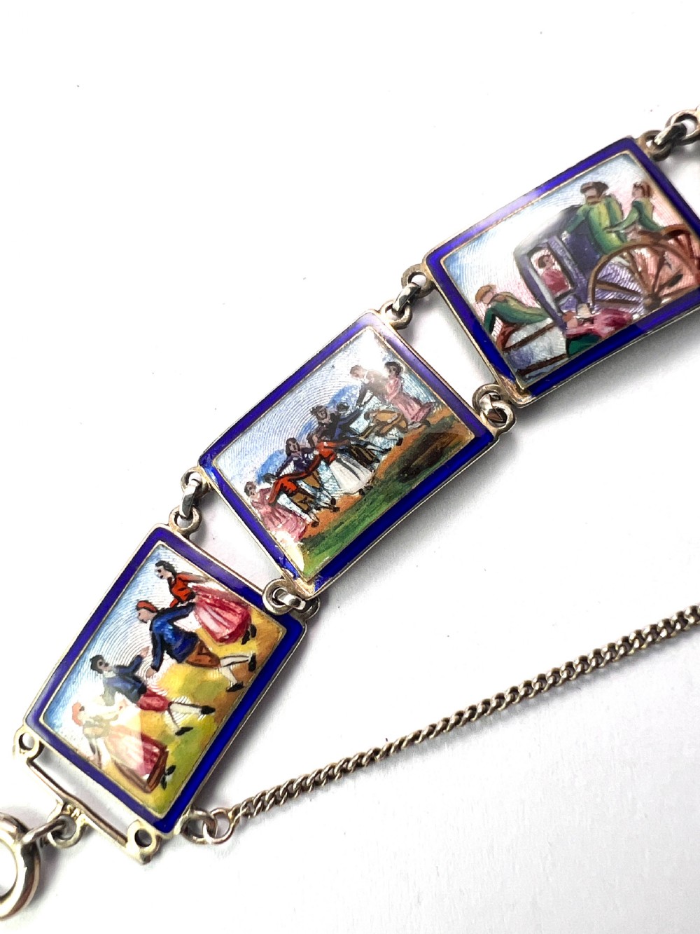 A vintage silver link bracelet featuring rectangular panels decorated with hand-painted miniature genre scenes bordered in cobalt blue enamel. View II