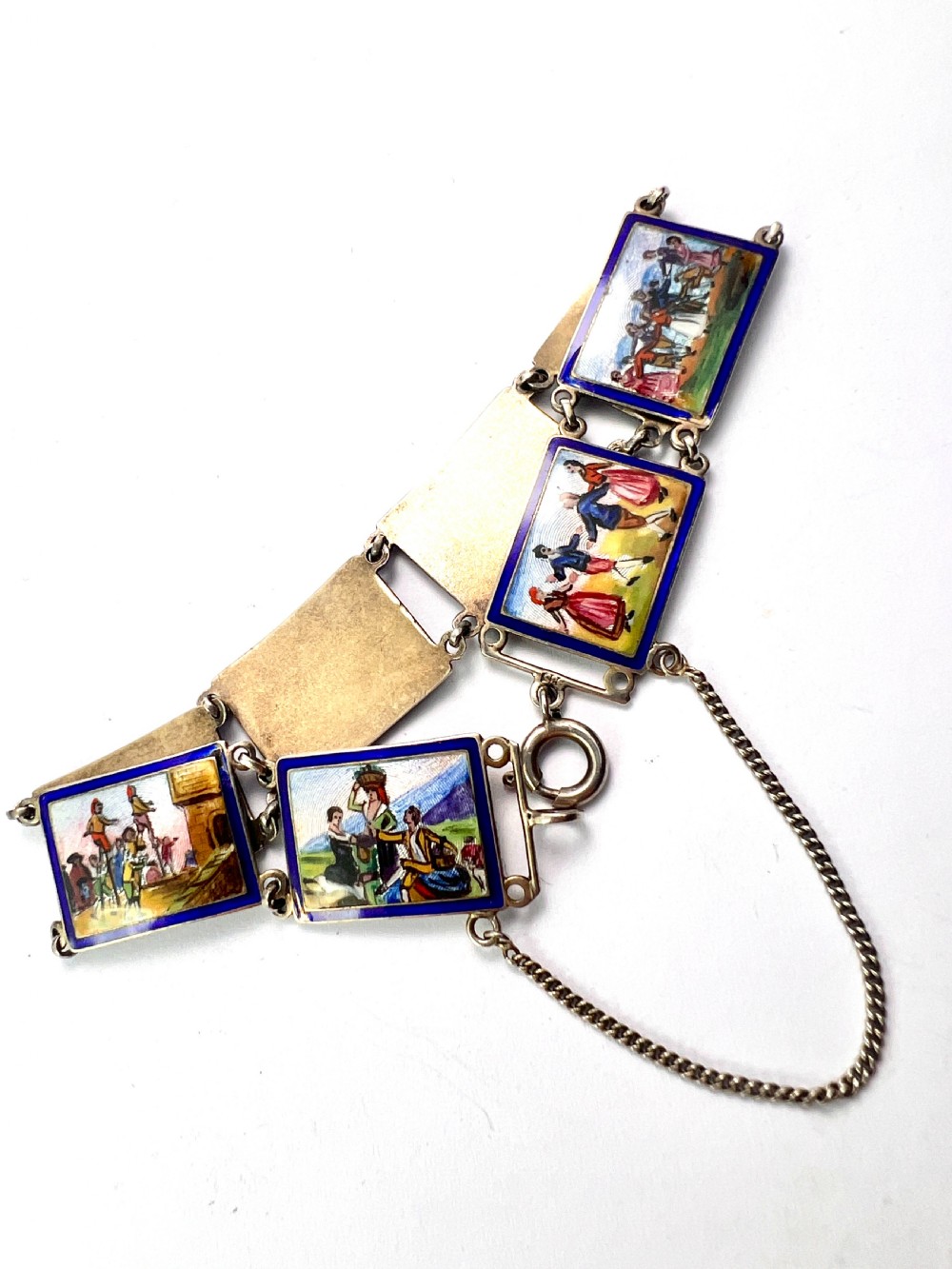 A vintage silver link bracelet featuring rectangular panels decorated with hand-painted miniature genre scenes bordered in cobalt blue enamel. View IV