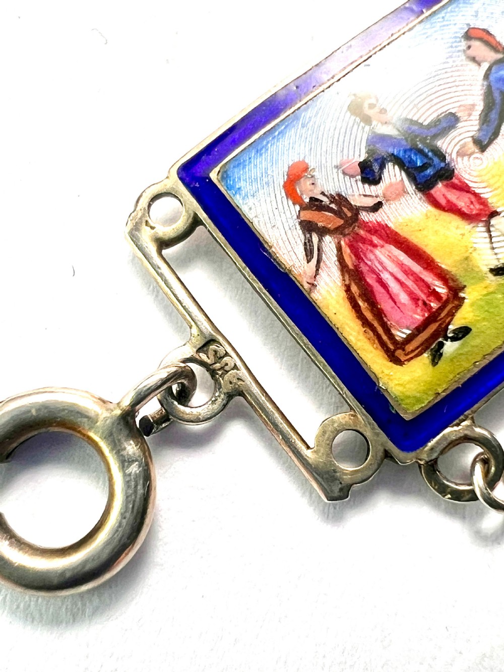 A vintage silver link bracelet featuring rectangular panels decorated with hand-painted miniature genre scenes bordered in cobalt blue enamel. View VII