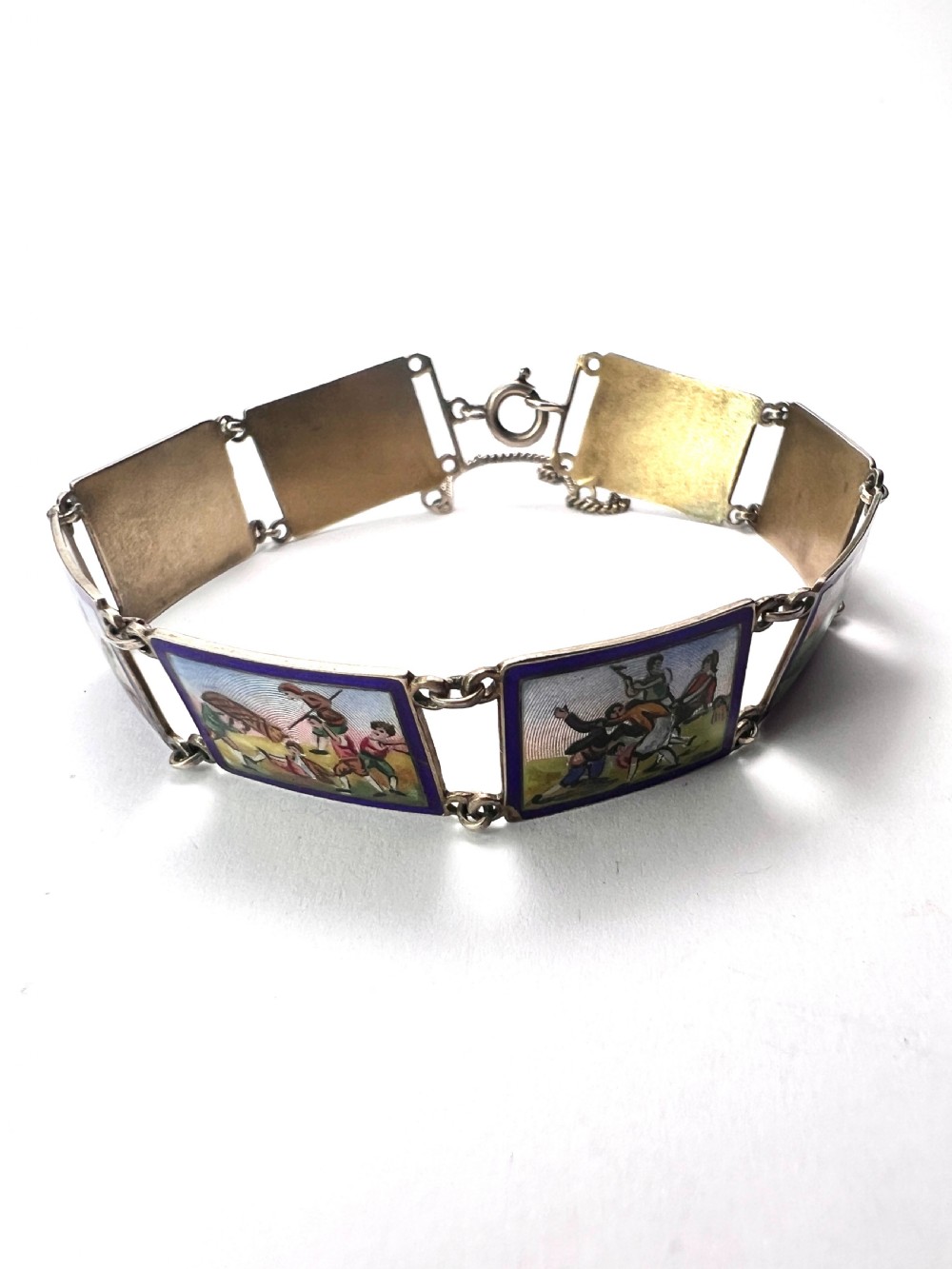 A vintage silver link bracelet featuring rectangular panels decorated with hand-painted miniature genre scenes bordered in cobalt blue enamel. View VIII