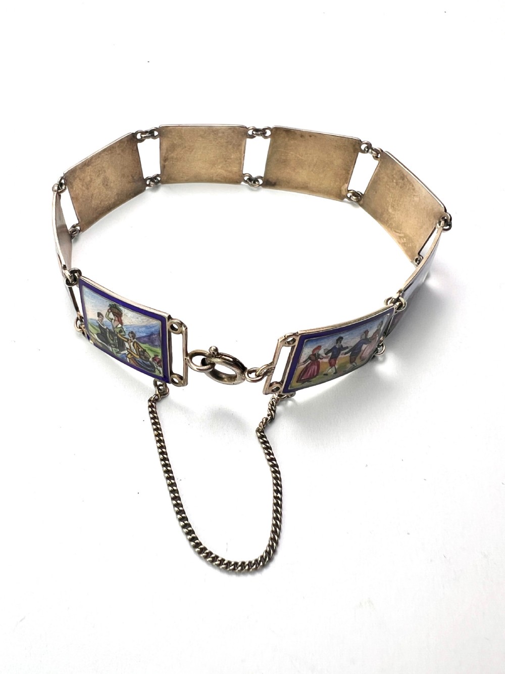 A vintage silver link bracelet featuring rectangular panels decorated with hand-painted miniature genre scenes bordered in cobalt blue enamel. View IX