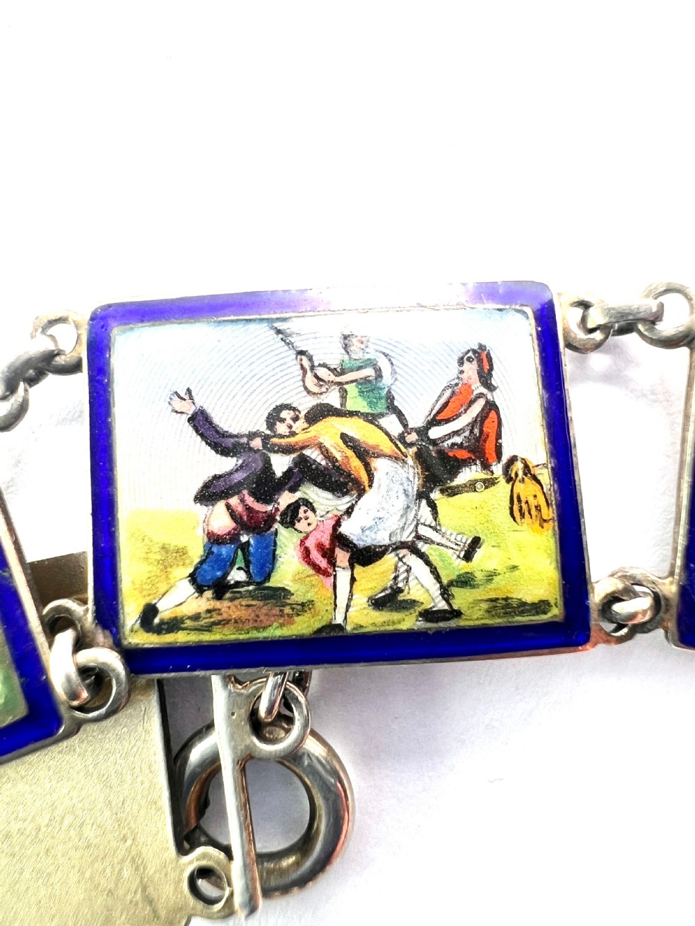A vintage silver link bracelet featuring rectangular panels decorated with hand-painted miniature genre scenes bordered in cobalt blue enamel. View XI