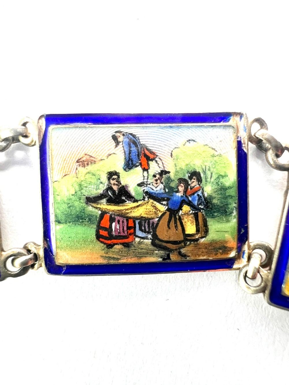 A vintage silver link bracelet featuring rectangular panels decorated with hand-painted miniature genre scenes bordered in cobalt blue enamel. View XII