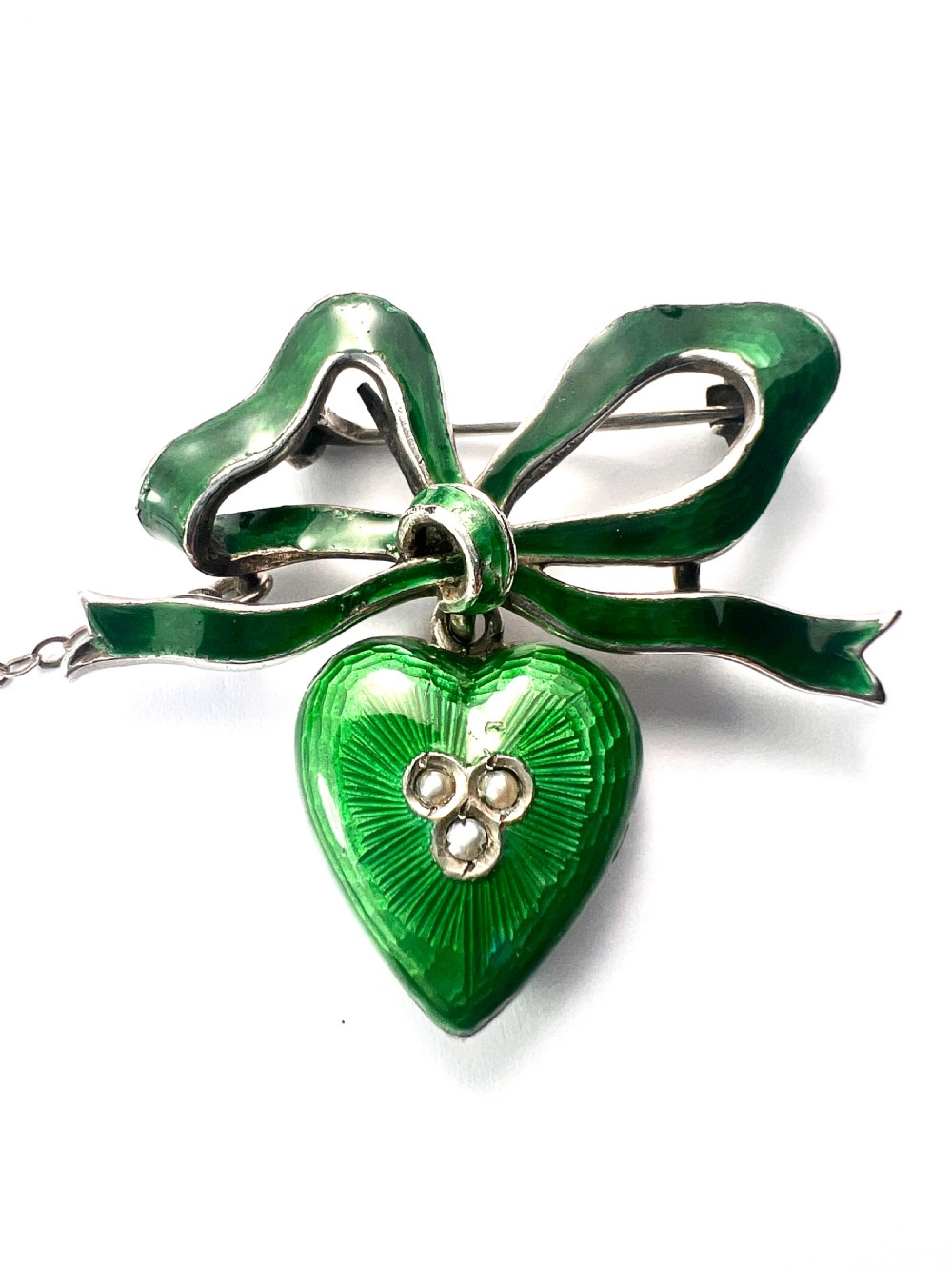An antique silver brooch featuring a green translucent enamel ribbon bow with a hanging green enamel heart drop set with three small seed pearls. View III