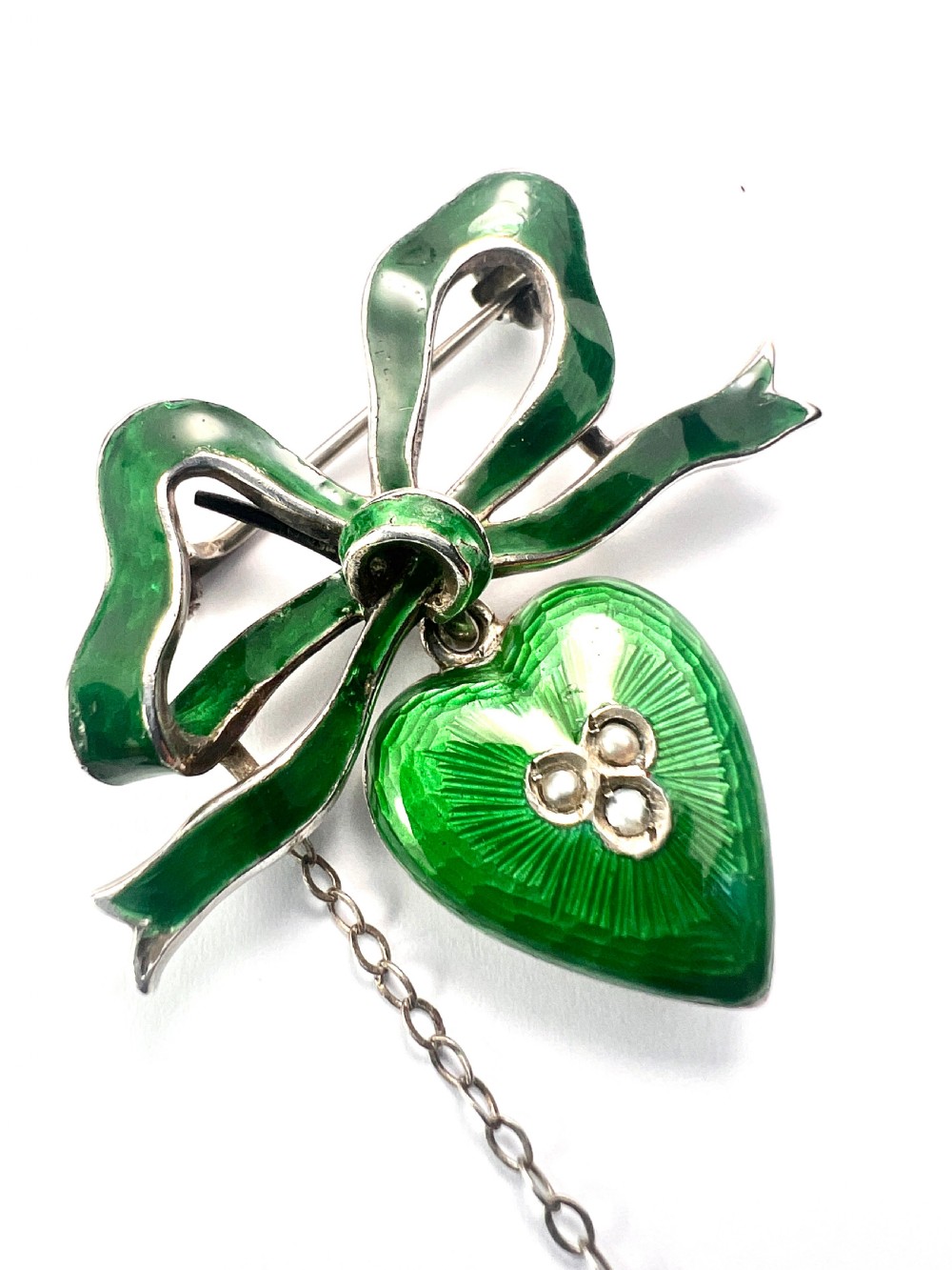 An antique silver brooch featuring a green translucent enamel ribbon bow with a hanging green enamel heart drop set with three small seed pearls. View IV