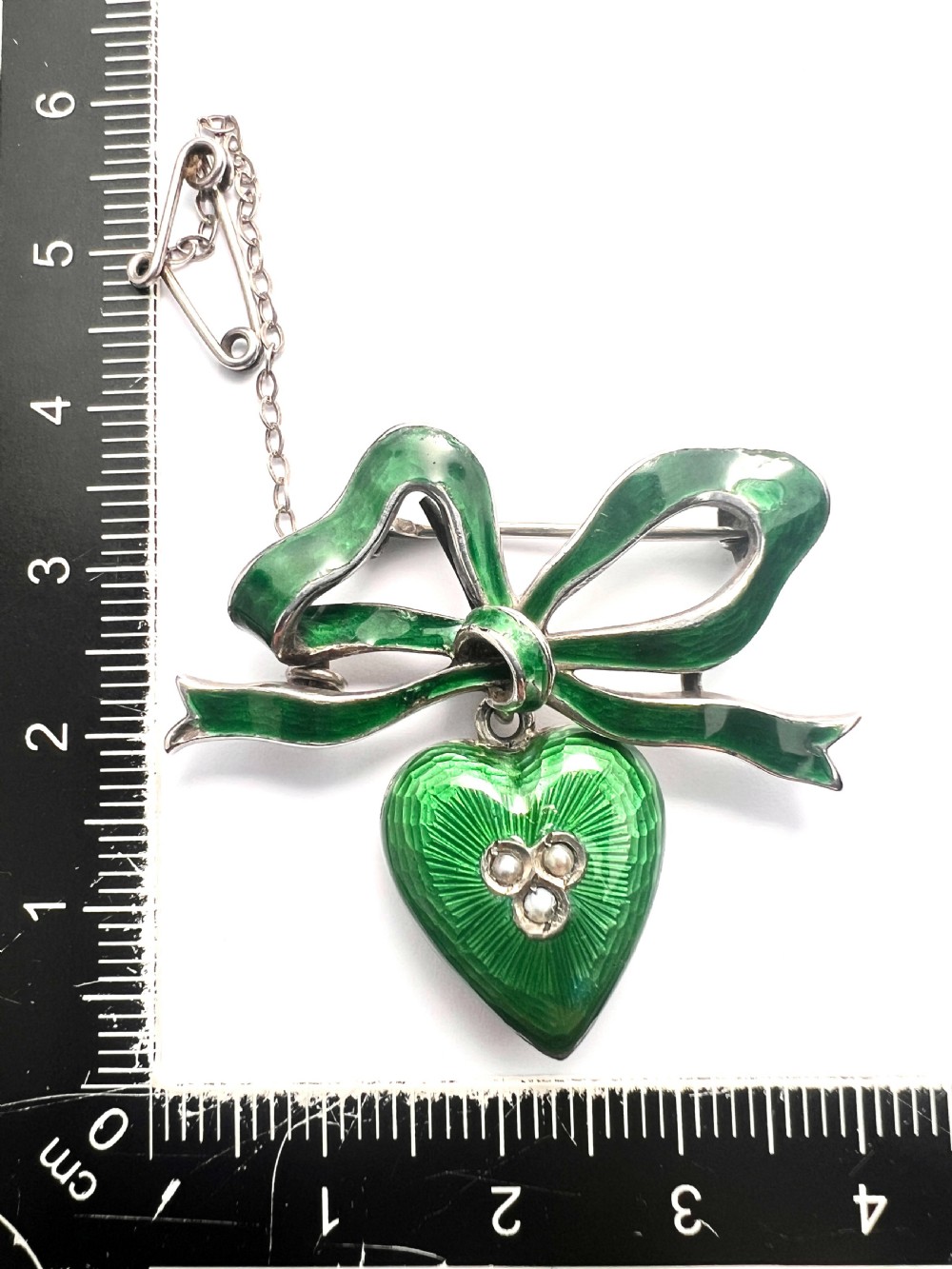 An antique silver brooch featuring a green translucent enamel ribbon bow with a hanging green enamel heart drop set with three small seed pearls. View VII