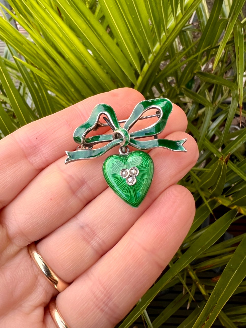 An antique silver brooch featuring a green translucent enamel ribbon bow with a hanging green enamel heart drop set with three small seed pearls. View VIII