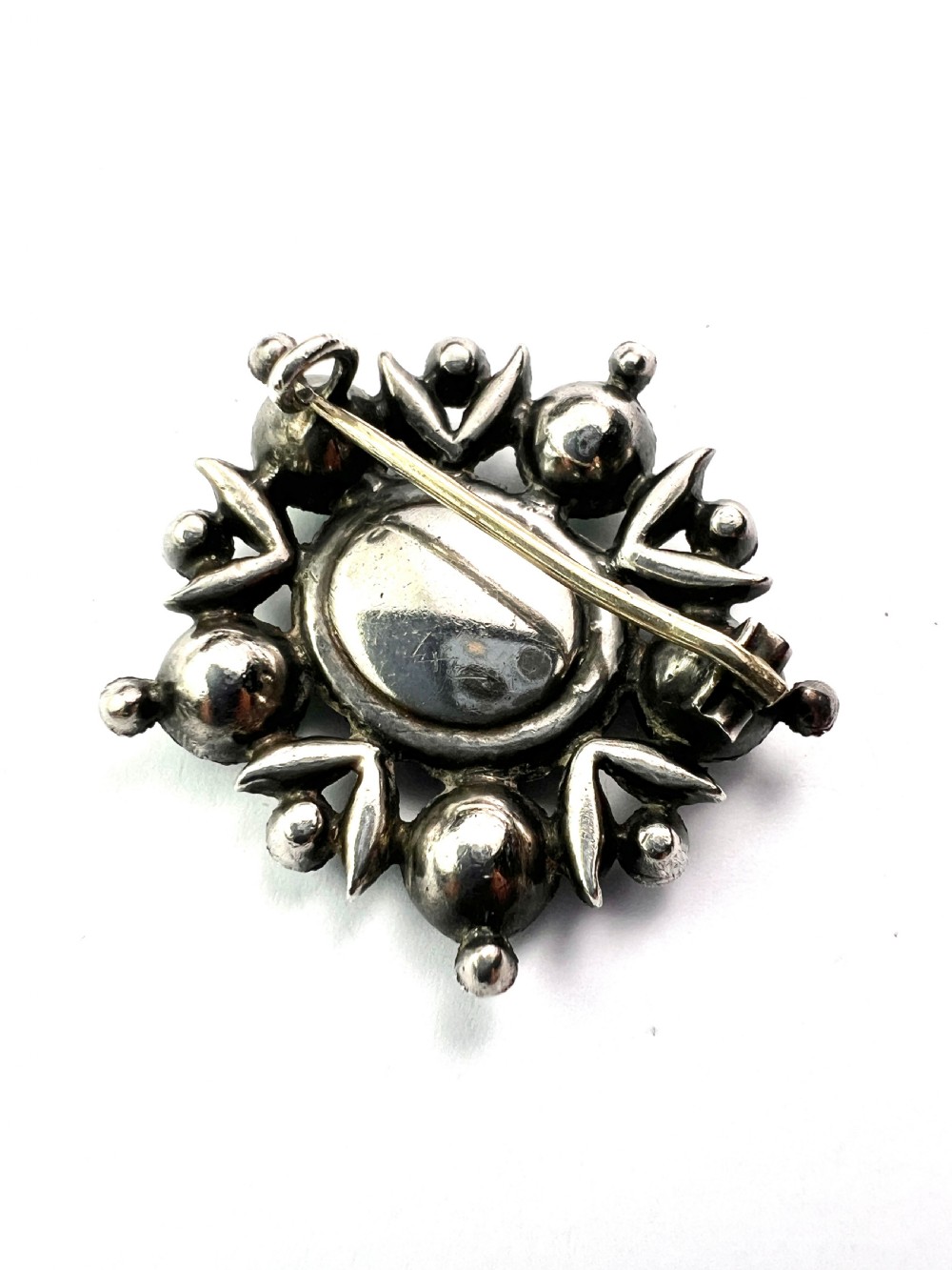 A silver cluster brooch featuring an oval green paste stone at the centre, encircled by smaller clear stones and outer green paste stones. View V