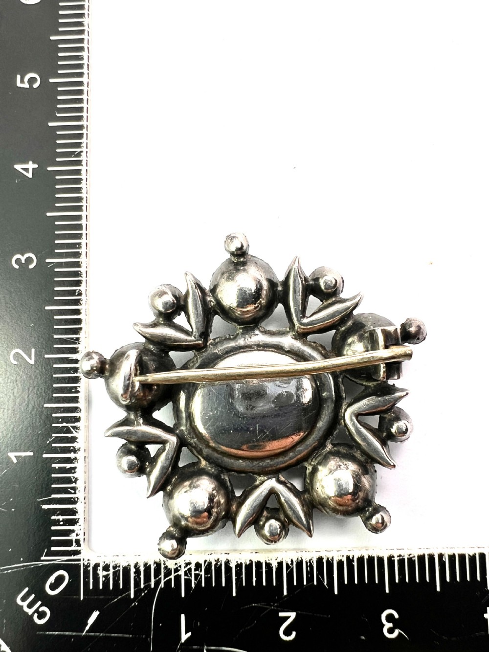 A silver cluster brooch featuring an oval green paste stone at the centre, encircled by smaller clear stones and outer green paste stones. View VI