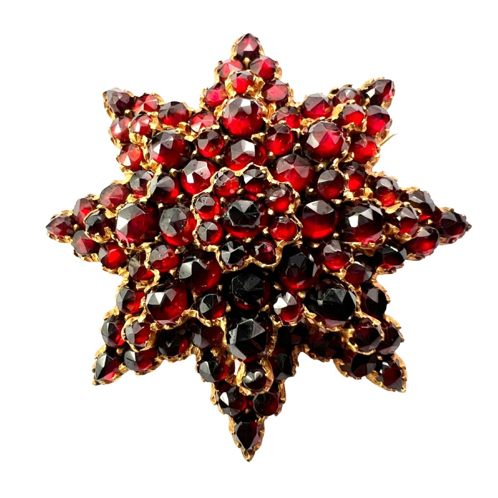 A multi-tiered starburst brooch closely set with faceted deep red rose-cut garnets in a gilded claw setting.