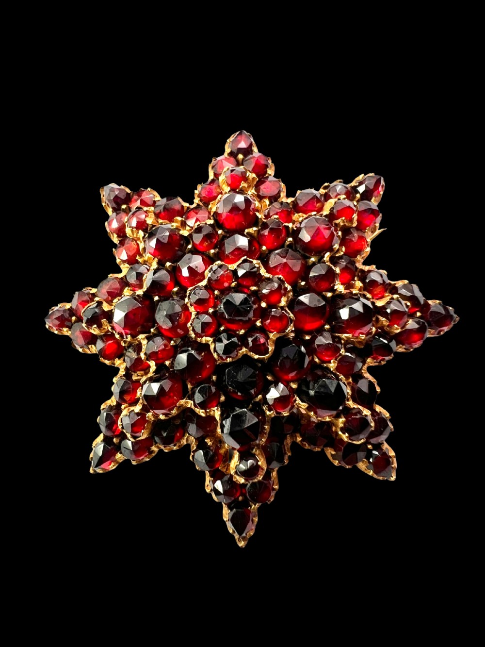 A multi-tiered starburst brooch closely set with faceted deep red rose-cut garnets in a gilded claw setting. View II