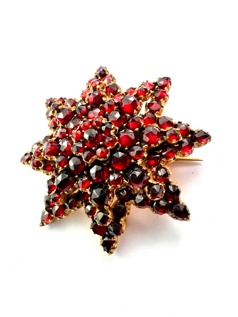 A multi-tiered starburst brooch closely set with faceted deep red rose-cut garnets in a gilded claw setting. View III