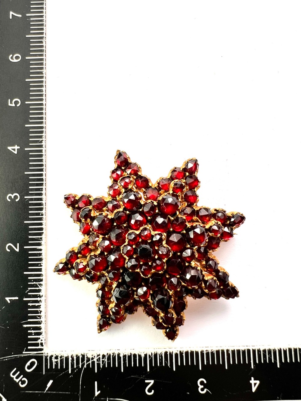 A multi-tiered starburst brooch closely set with faceted deep red rose-cut garnets in a gilded claw setting. View IV