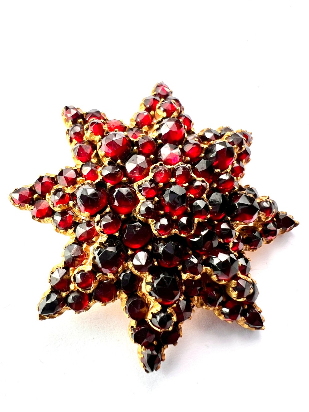 A multi-tiered starburst brooch closely set with faceted deep red rose-cut garnets in a gilded claw setting. View V
