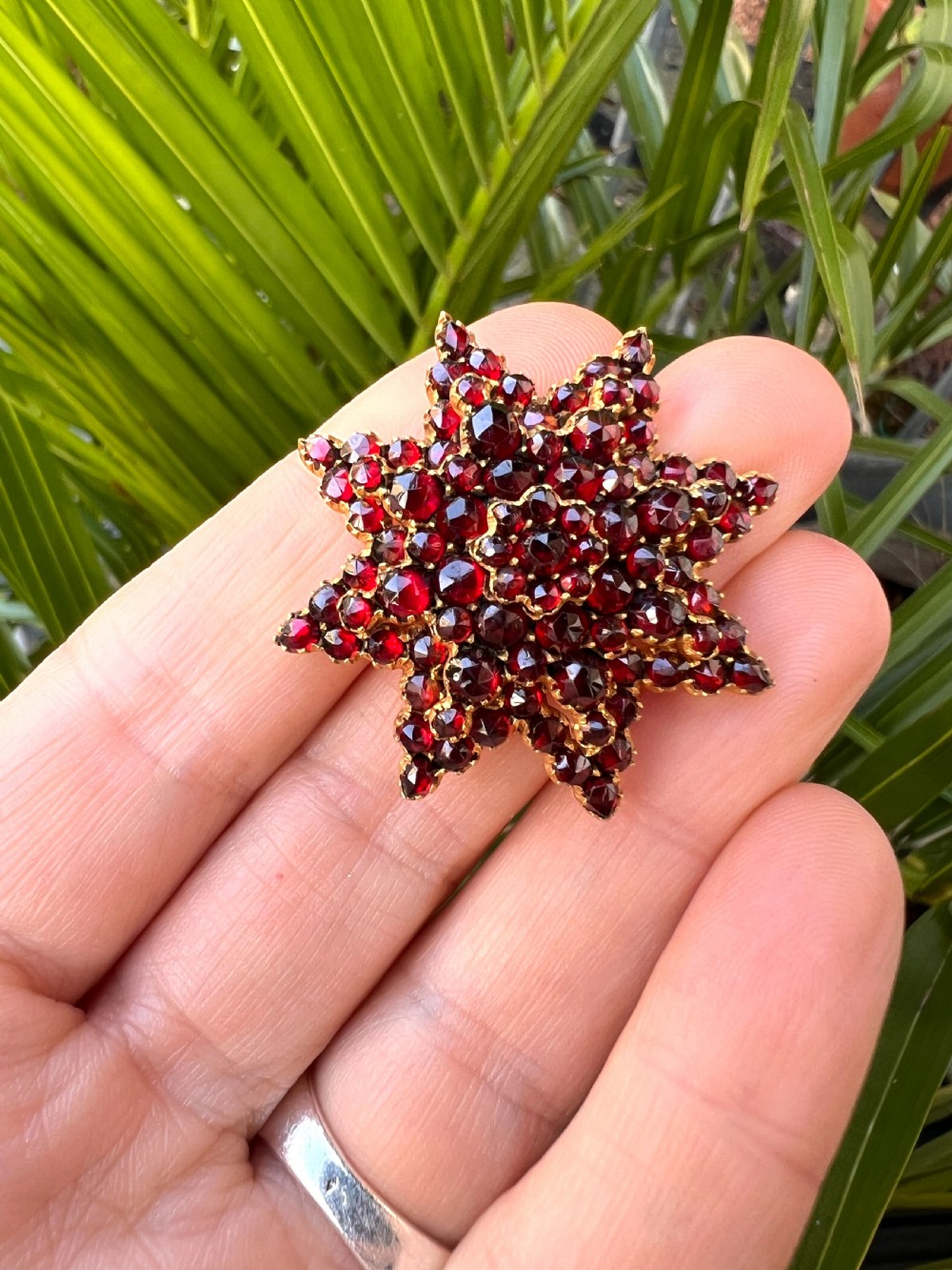 A multi-tiered starburst brooch closely set with faceted deep red rose-cut garnets in a gilded claw setting. View VI