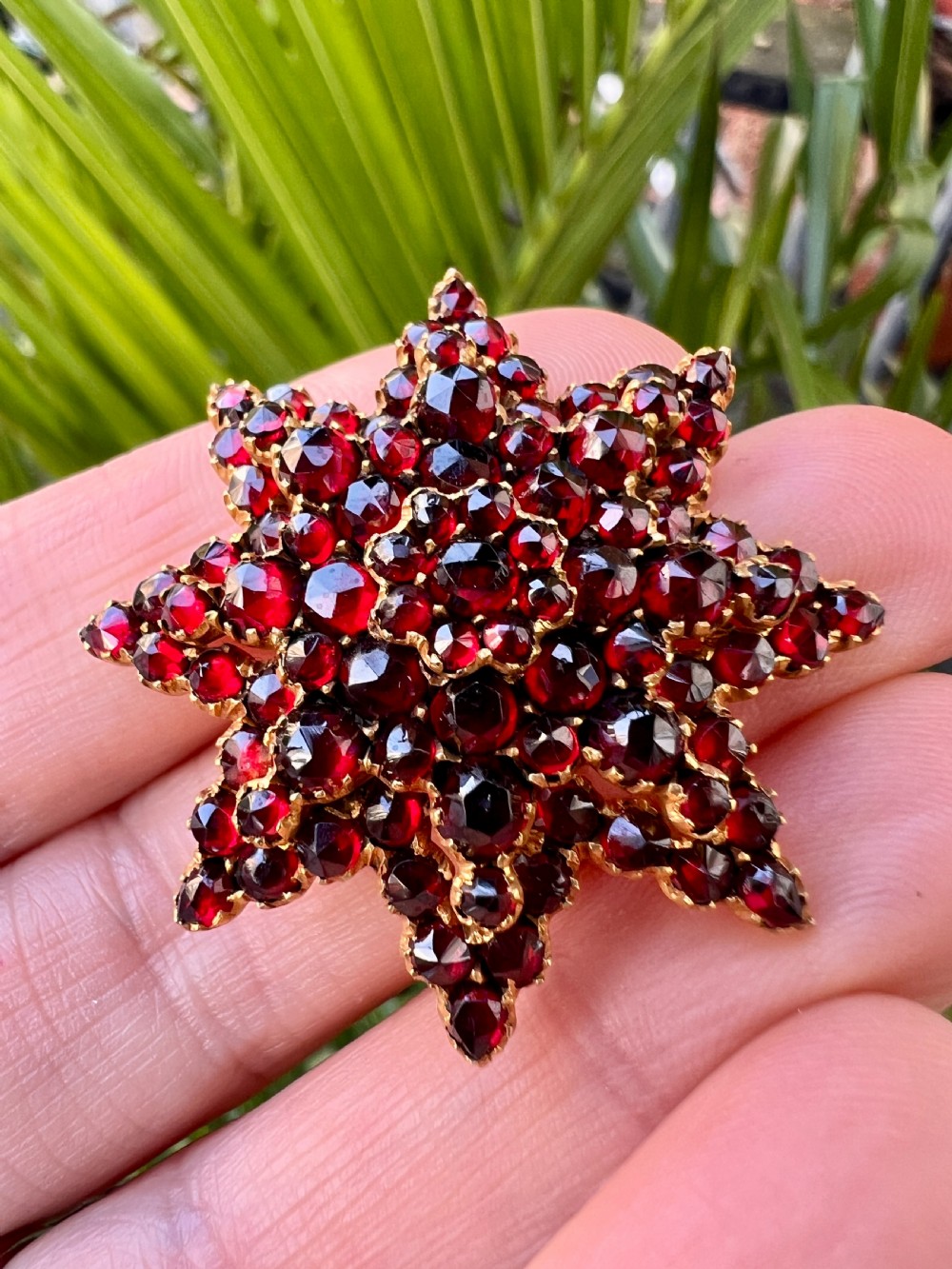 A multi-tiered starburst brooch closely set with faceted deep red rose-cut garnets in a gilded claw setting. View VIII
