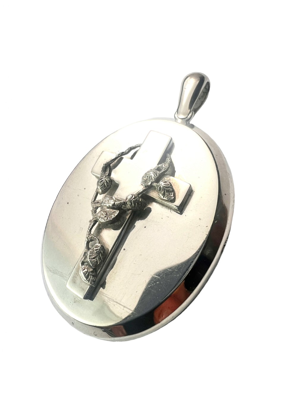 A large oval silver locket featuring a central raised crucifix motif draped with sculpted ivy foliage, fitted with an oval bail at the top. View II