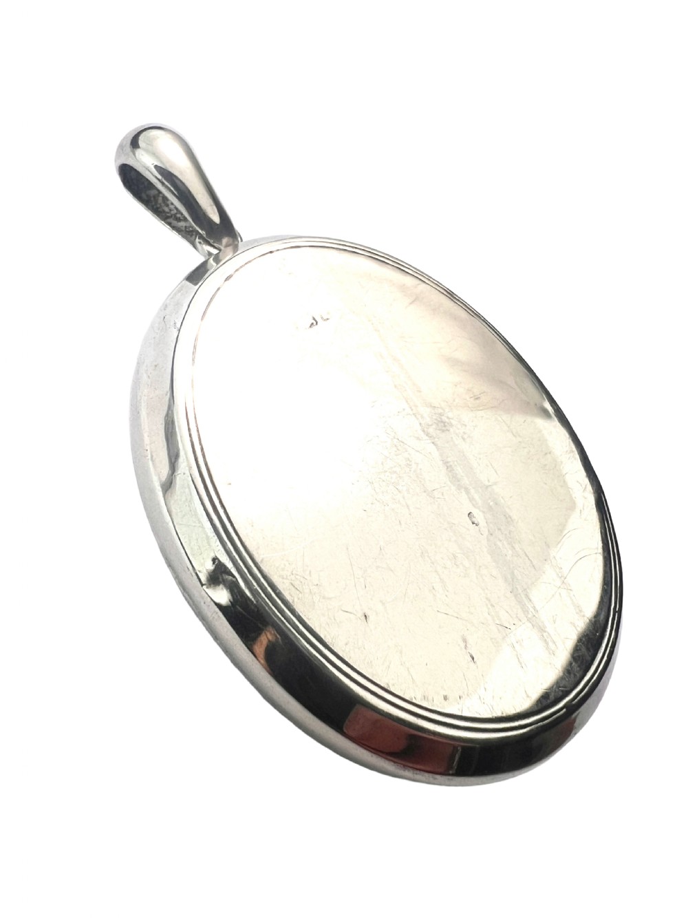A large oval silver locket featuring a central raised crucifix motif draped with sculpted ivy foliage, fitted with an oval bail at the top. View III