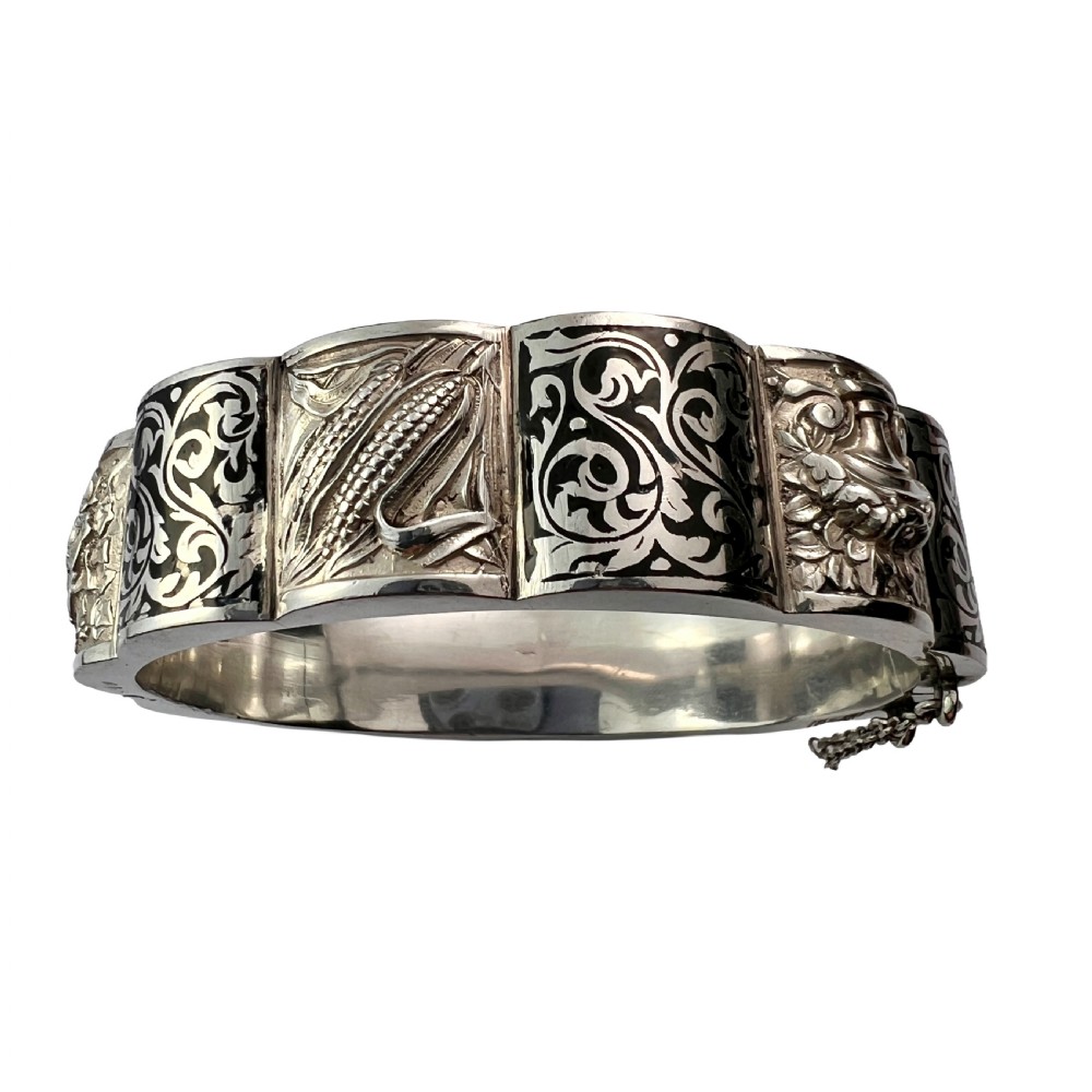 A vintage Portuguese silver hinged cuff bangle featuring engraved foliate scrollwork and corn motifs with dark niello detailing and a safety chain.