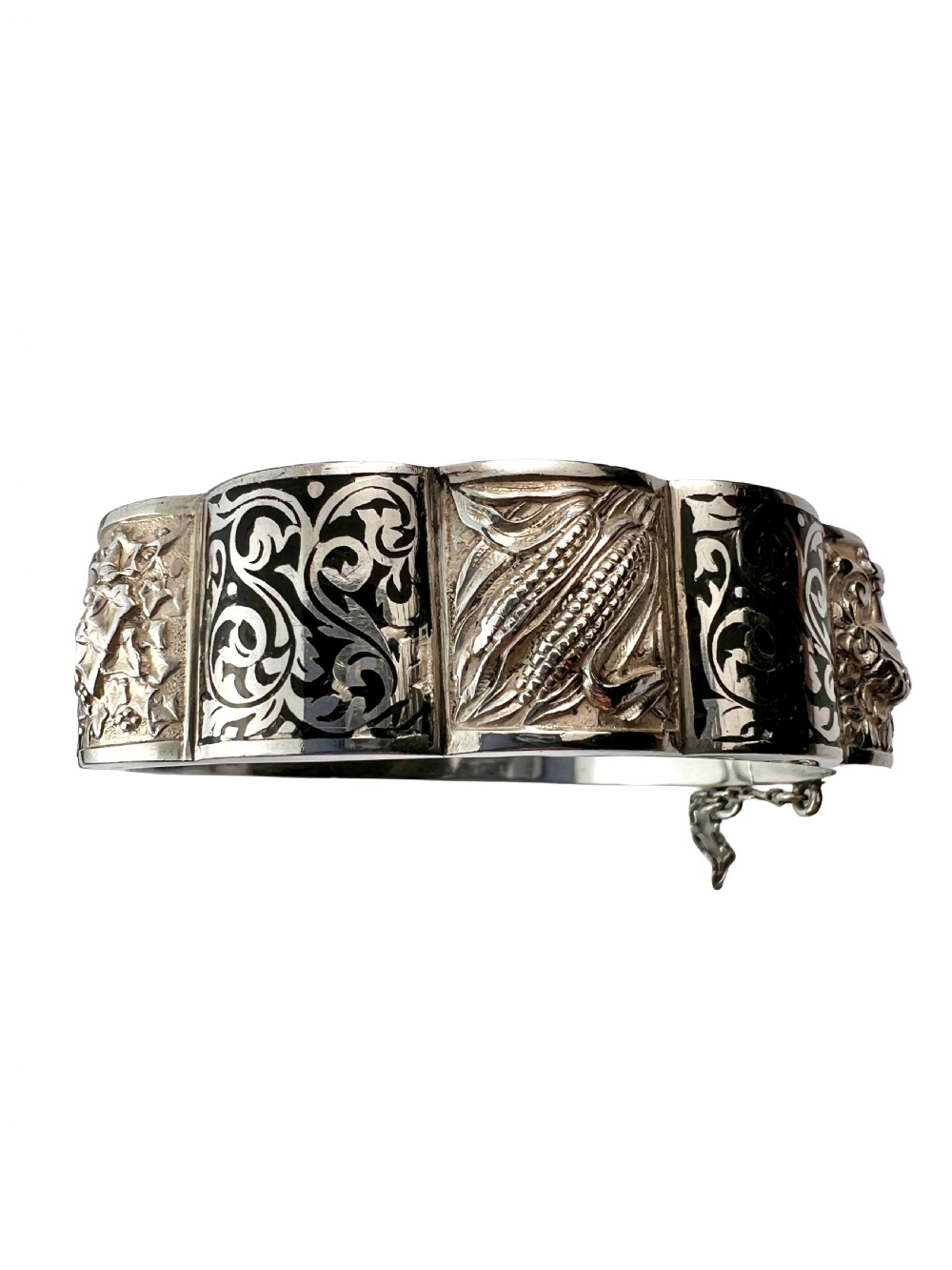 A vintage Portuguese silver hinged cuff bangle featuring engraved foliate scrollwork and corn motifs with dark niello detailing and a safety chain. View II