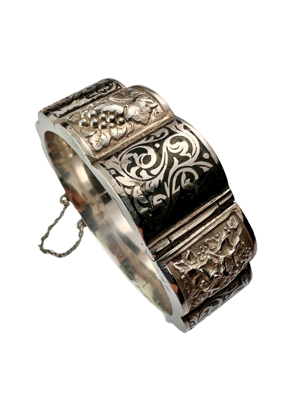 A vintage Portuguese silver hinged cuff bangle featuring engraved foliate scrollwork and corn motifs with dark niello detailing and a safety chain. View III