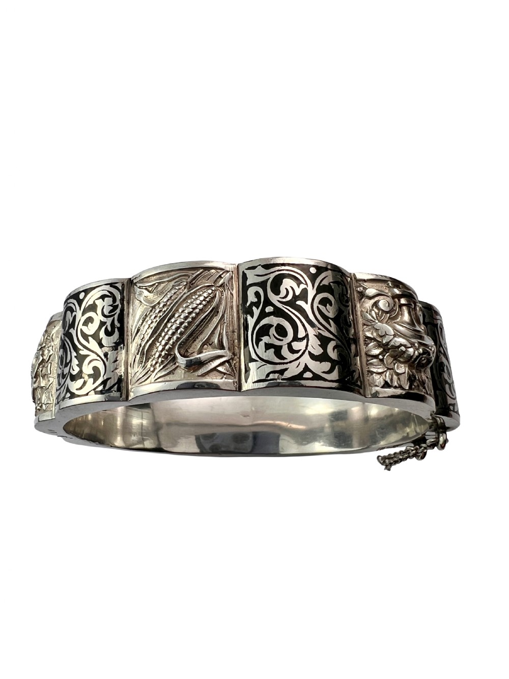 A vintage Portuguese silver hinged cuff bangle featuring engraved foliate scrollwork and corn motifs with dark niello detailing and a safety chain. View VI