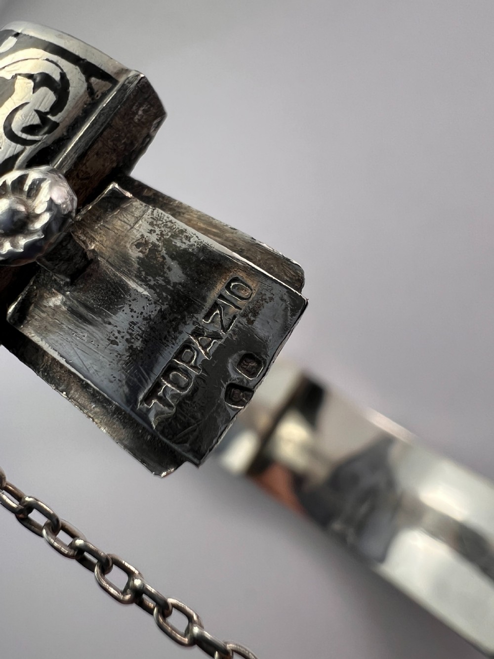 A vintage Portuguese silver hinged cuff bangle featuring engraved foliate scrollwork and corn motifs with dark niello detailing and a safety chain. View VIII