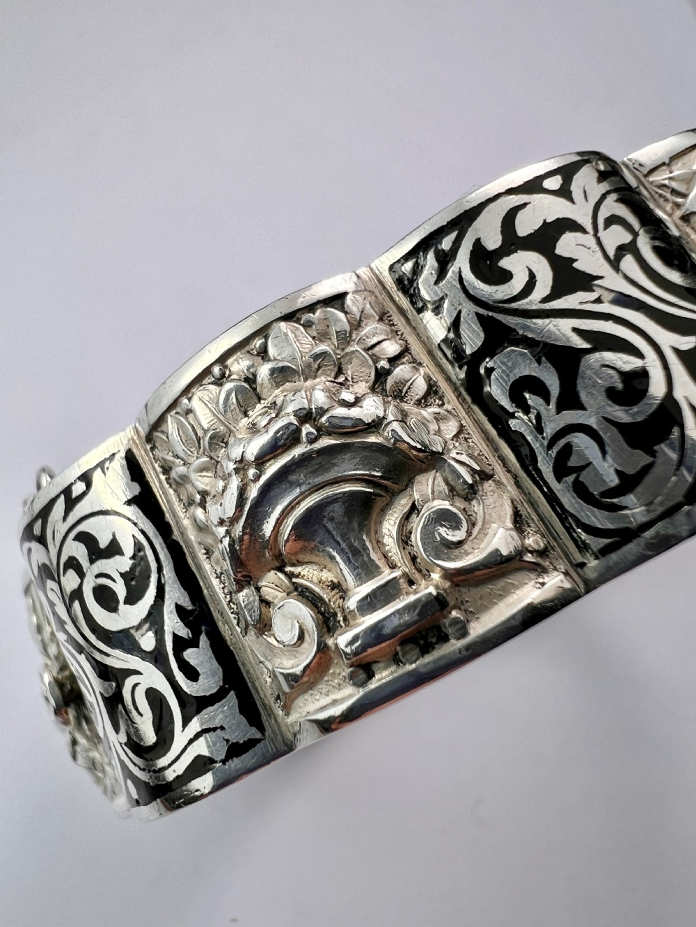 A vintage Portuguese silver hinged cuff bangle featuring engraved foliate scrollwork and corn motifs with dark niello detailing and a safety chain. View X