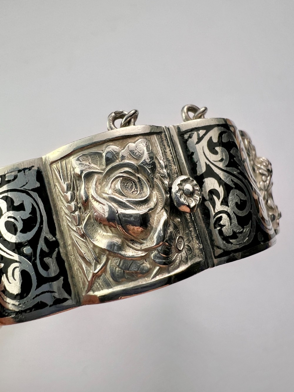 A vintage Portuguese silver hinged cuff bangle featuring engraved foliate scrollwork and corn motifs with dark niello detailing and a safety chain. View XI