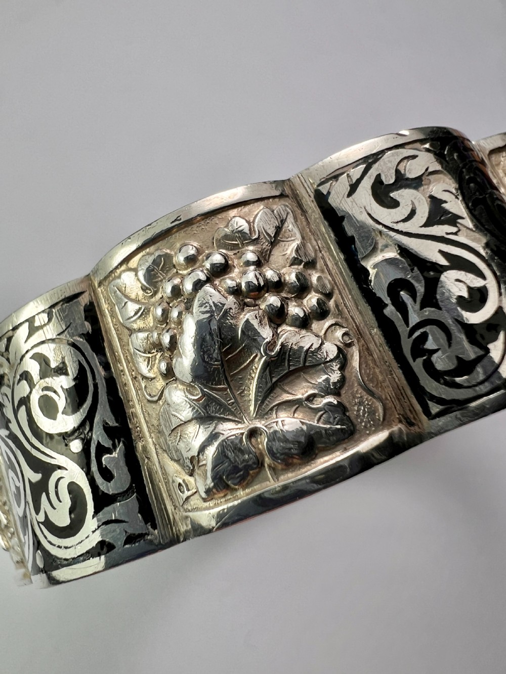 A vintage Portuguese silver hinged cuff bangle featuring engraved foliate scrollwork and corn motifs with dark niello detailing and a safety chain. View XII