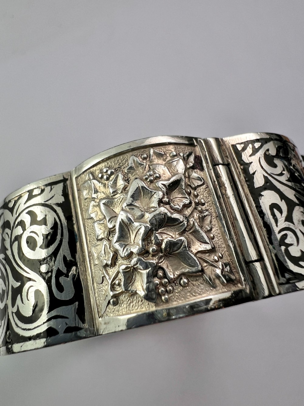 A vintage Portuguese silver hinged cuff bangle featuring engraved foliate scrollwork and corn motifs with dark niello detailing and a safety chain. View XIII